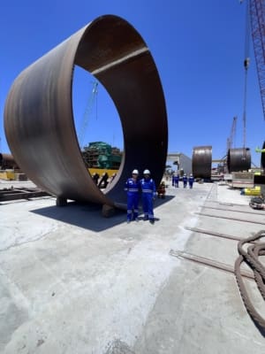 Taylor Hopkinson QAQC inspectors in front of an enormous offshore wind turbine tower component on its side in a fabrication yard in the UAE.