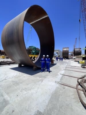 Taylor Hopkinson QAQC inspectors in front of an enormous offshore wind turbine tower component on its side in a fabrication yard in the UAE.