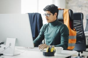 Young male renewable energy engineering specialist at his desk looking at computer monitor. Businessman working on computer sitting at engineering office desk.